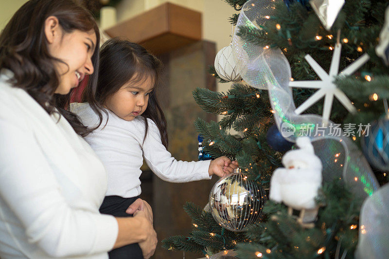 Young girl and her mom put decorations on the Christmas tree